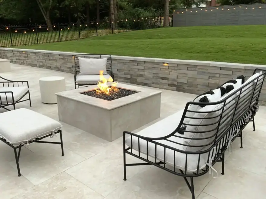 A square gas fire table on a travertine patio ringed with iron frame lounge seating at dusk
