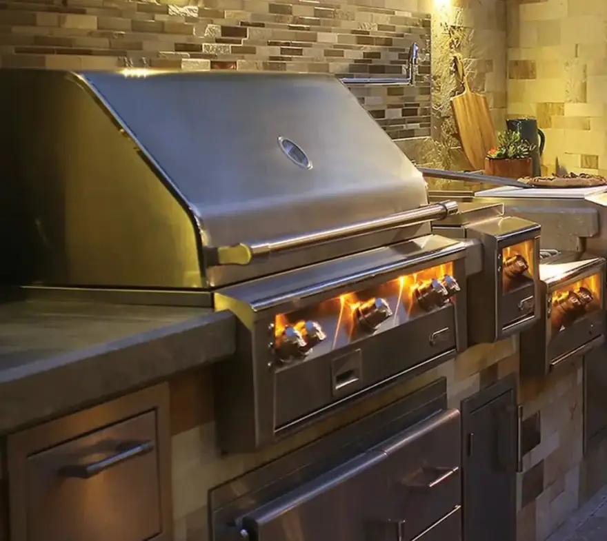 A built-in stainless steel grill set into a stone outdoor kitchen island