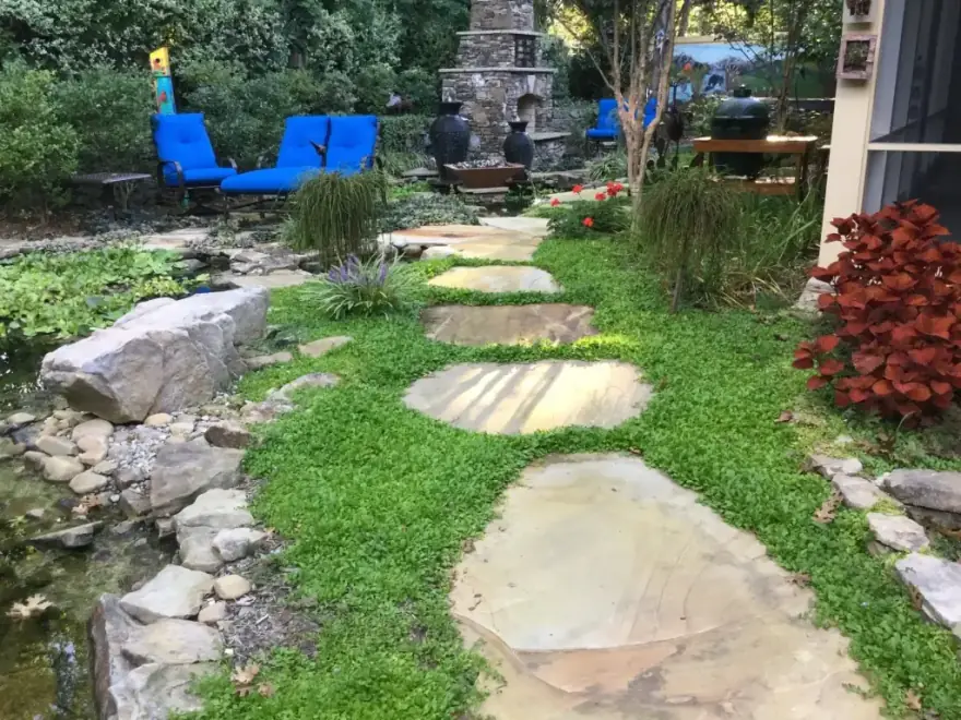 A woodland stepping stone path with a koi pond, stone outdoor fireplace and seating built by Allin Landscaping