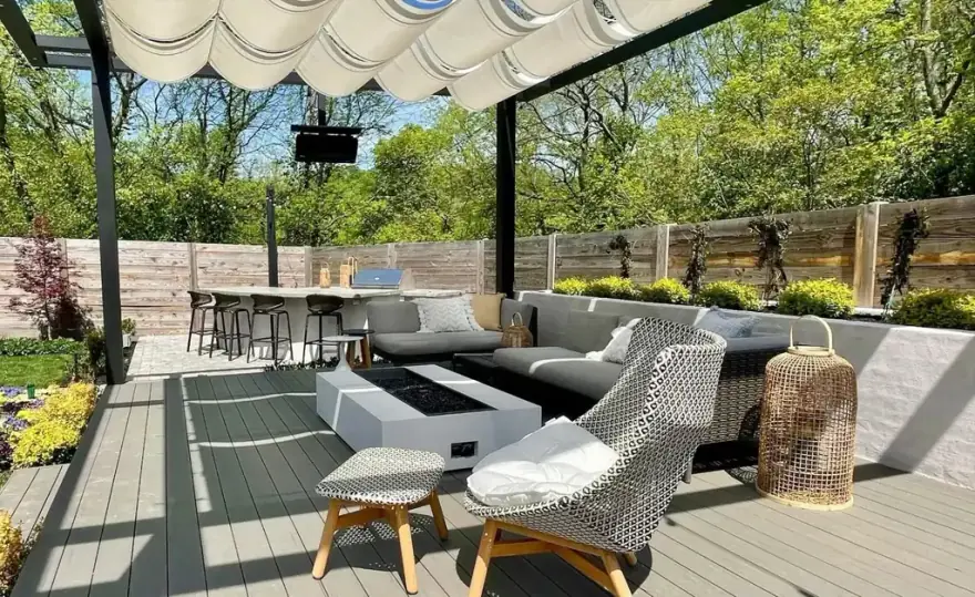 A covered outdoor living room with a retractable canopy, fire table, sectional seating and a full bar
